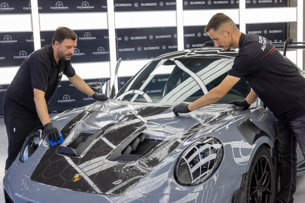 Aufziehen von PPF Schutzfolie auf Motorhaube von grauem Porsche GT3 RS durch zwei maennliche Facharbeiter